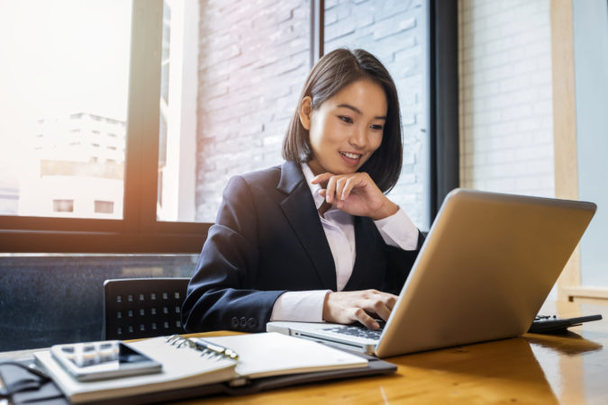 Closeup of businesswoman using laptop at office desk. She searching web or browsing information.