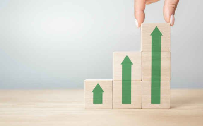 Business concept growth success process, Close up Businesswoman hand arranging wood cube with green arrow stacking as step stair. copy space, gray background