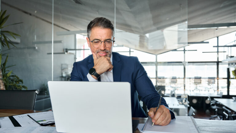 Middle aged business man executive watching webinar on laptop writing notes.